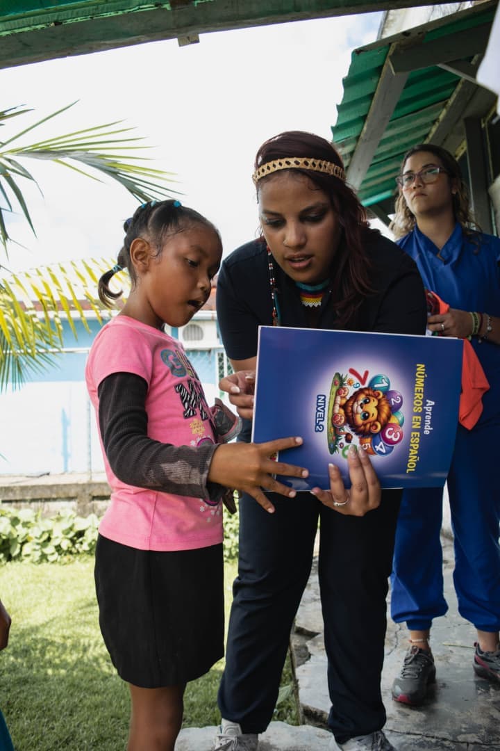 Voluntaria entregando material educativo a niña indígena